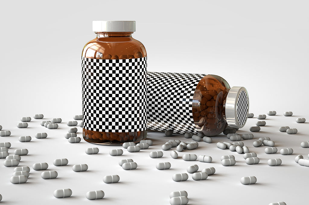 Two shiny glass amber supplement/vitamins bottle mock-up full of pills on a white surface with an editable label on the front of the bottle and lid. One Bottle is standing upright and the other bottle is on its side with the pills scattered out over the table